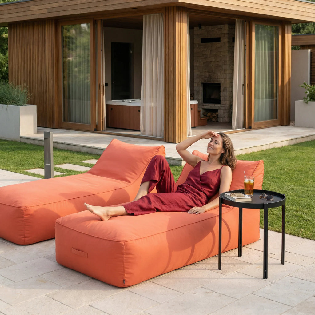Mulher relaxando em espreguiçadeira laranja Caraíva à beira de uma piscina com área de lazer ao fundo